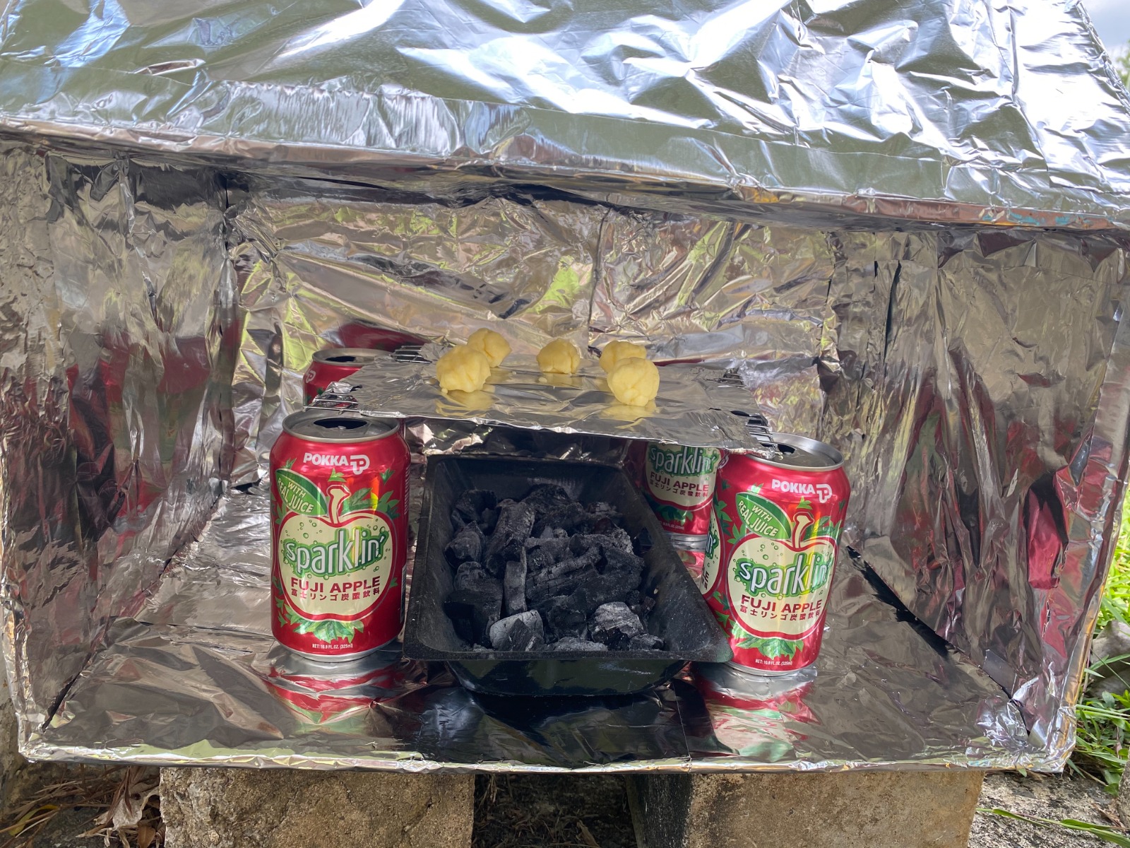 Close-up of a foil-lined DIY oven with drink cans inside